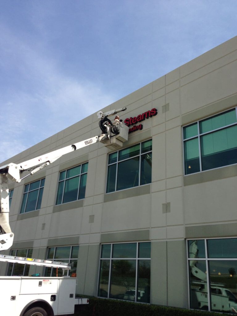 Priority Signs & Graphics expert installing outdoor sign on building in Dallas, TX